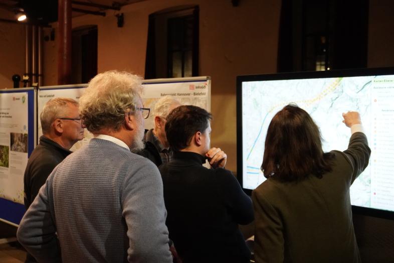 Menschen sehen sich auf einem großen Stand-Bildschirm eine Karte an.