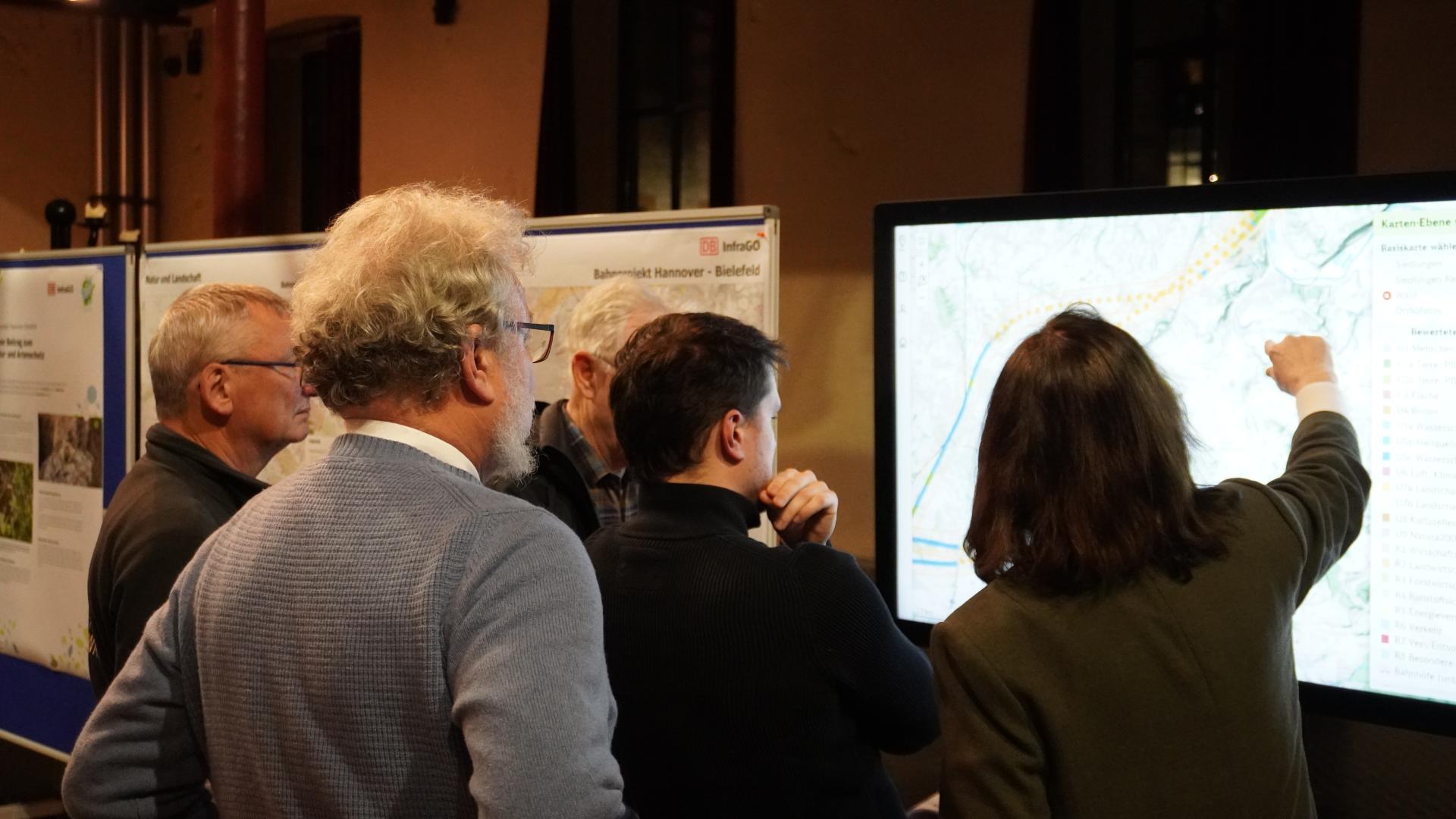 Menschen sehen sich auf einem großen Stand-Bildschirm eine Karte an.